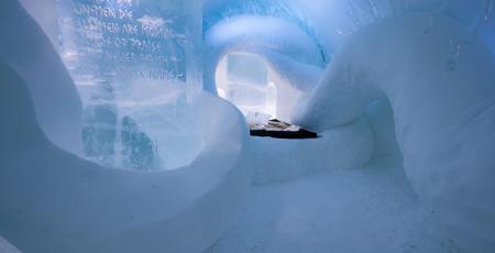sovrum med säng omgiven av is och snö i ishotelletus på vintern