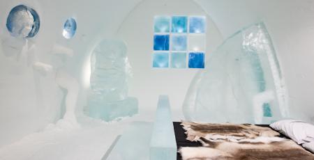 en säng med renskinn i ett vackert rum av is och snö på icehotel