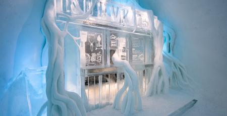 hot dog stand in ice covered by roots of snow inside Icehotelbed with reindeer hides in room with walls of snow in Icehotel