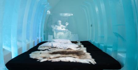 a bed covered with reindeer hides surrounded by ice in icehotel