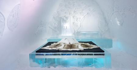 a bed covered with reindeer hides surrounded by beautiful ice art at icehotel