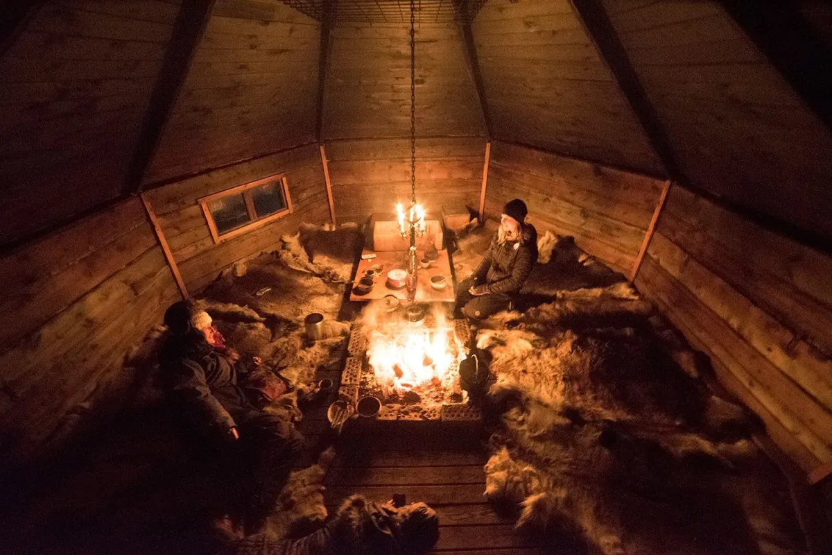 two people in a cabin, sitting on reindeer hides in front of the fire