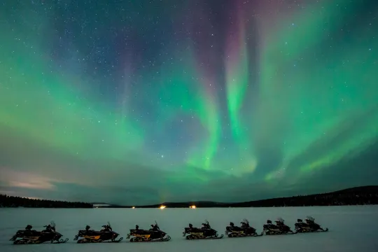snowmobiles in the wild surrounded bu the northern lights
